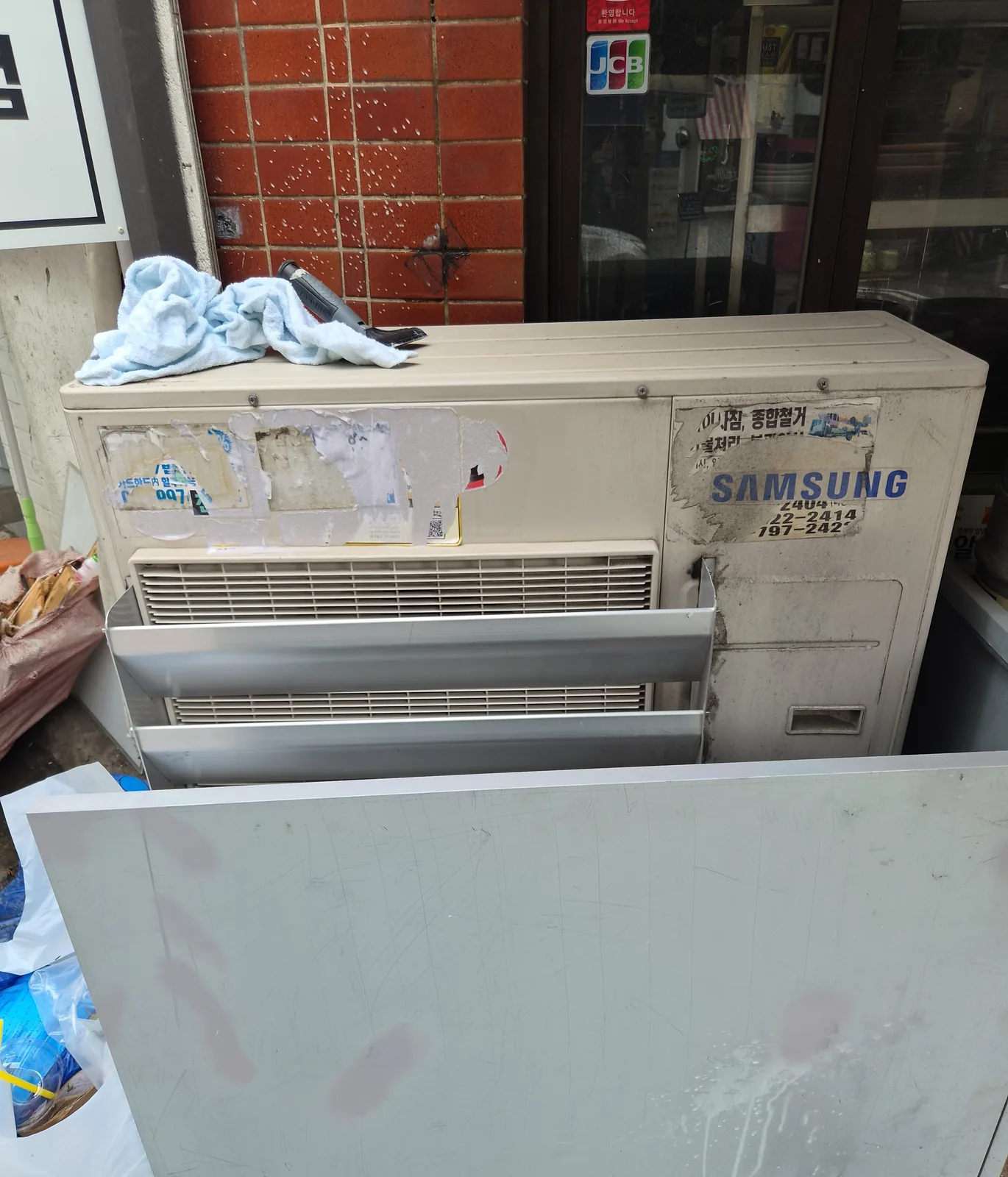 스티커와 접착 잔여물을 걷어낸 실외기 상판 — 제거 후, 전용 스크래퍼와 타월