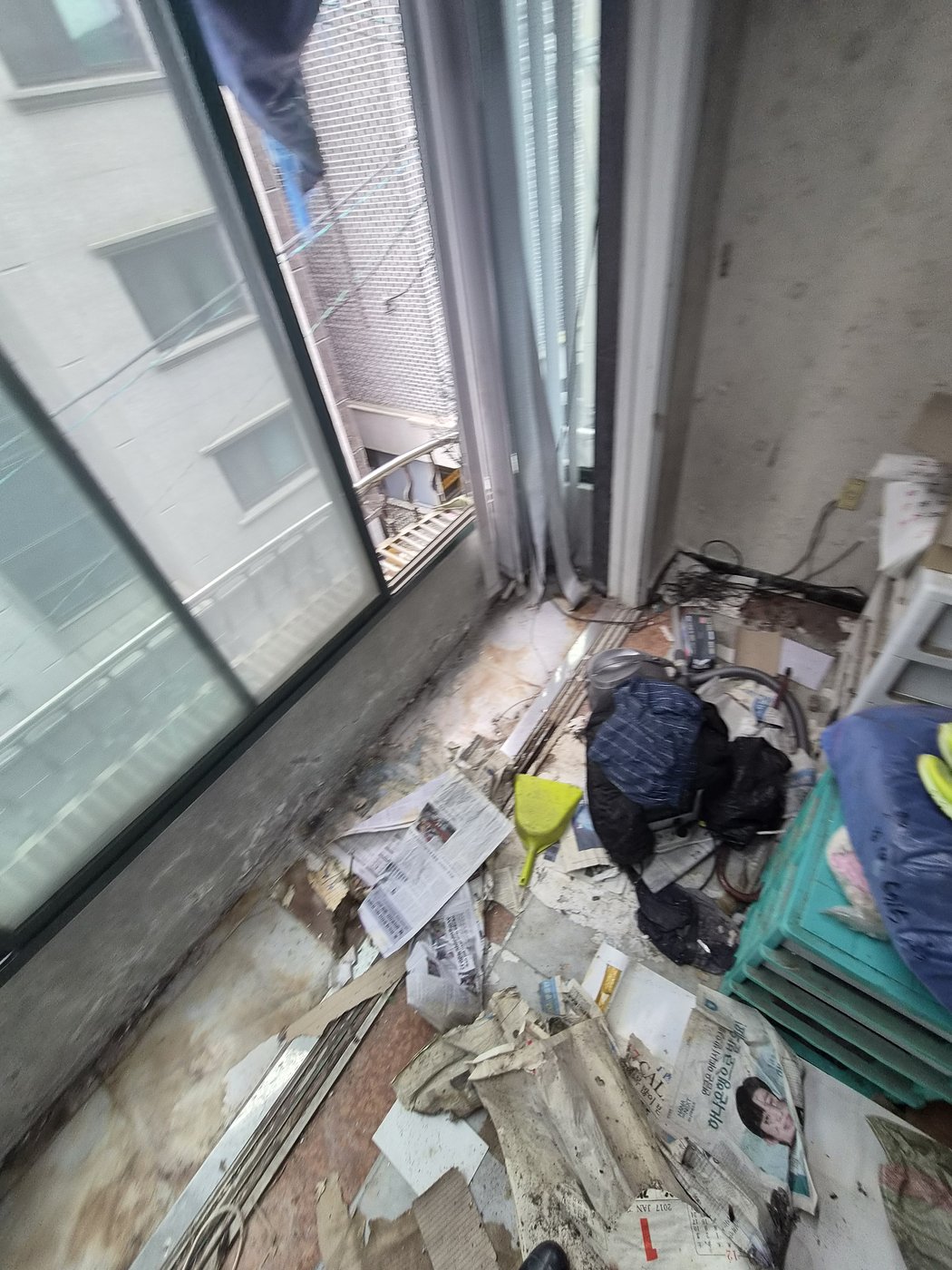 신문지와 잡동사니가 바닥을 덮은 방치된 집 베란다의 착수 전 상태