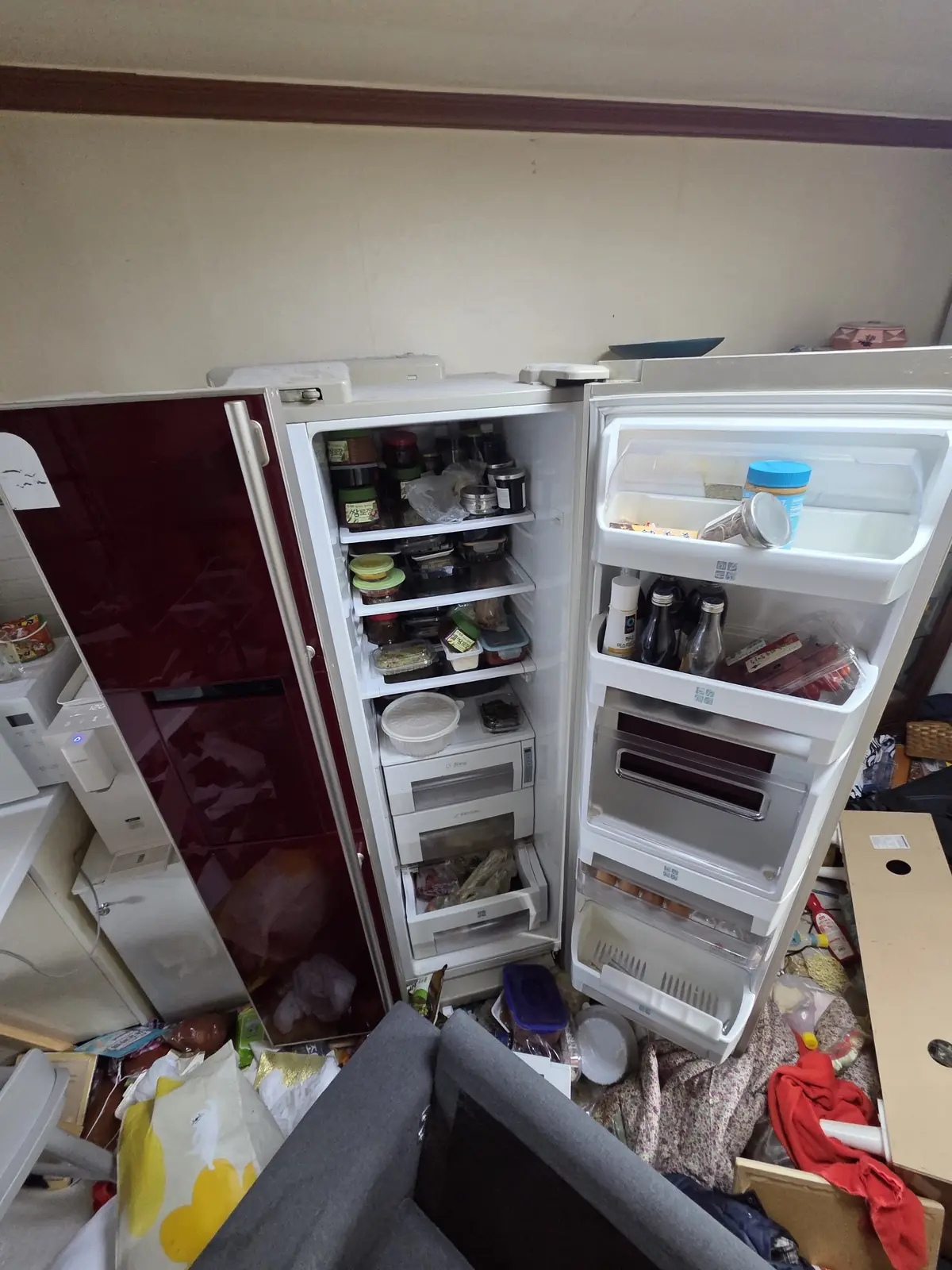 문을 연 냉장고 두 대 내부와 주변 바닥에 쌓인 물건들 — 냉장고 내용물 분류가 필요한 상태