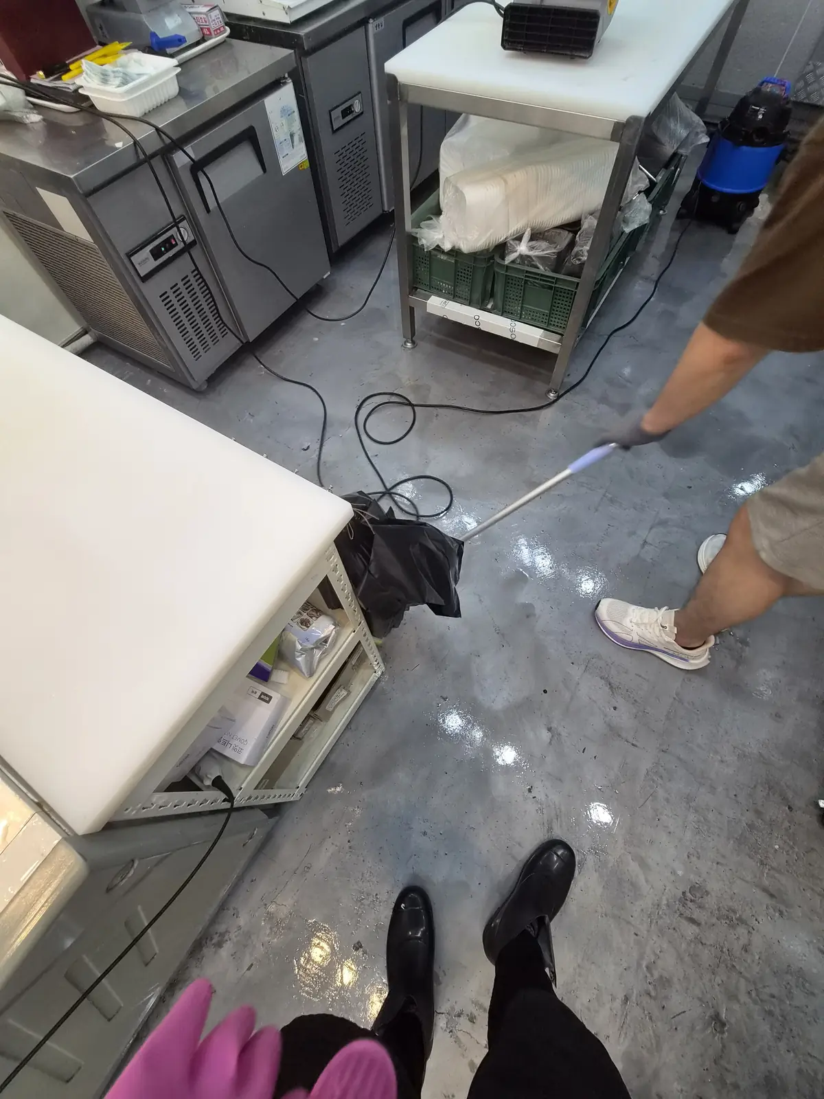 정육점 바닥의 잔여 오수를 두 사람이 나눠 밀어내며 세정하는 작업 중 장면