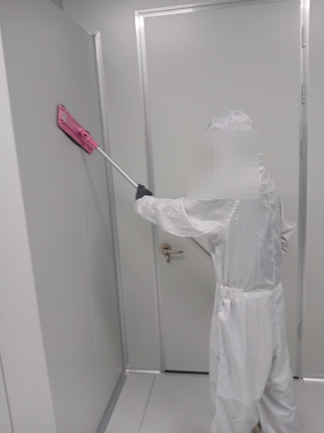 방진복을 입은 작업자가 클린룸 벽체 패널을 극세사 플랫 몹으로 닦는 모습