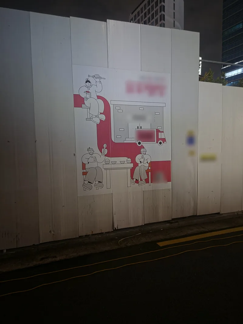 밤에 조명을 받은 공사장 흰 가림막에 붙은 대형 그림 홍보 시트, 문구와 전단은 흐림 처리