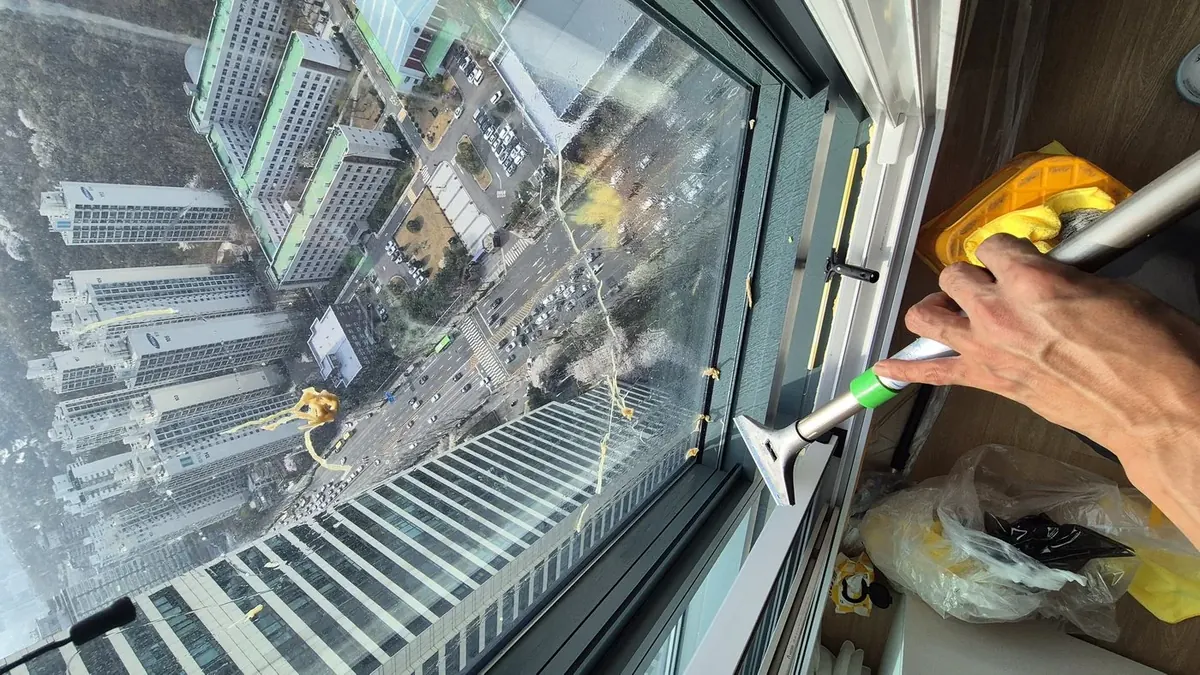 고층 창문 열어 바깥면 세정 중 — 스퀴지 작업