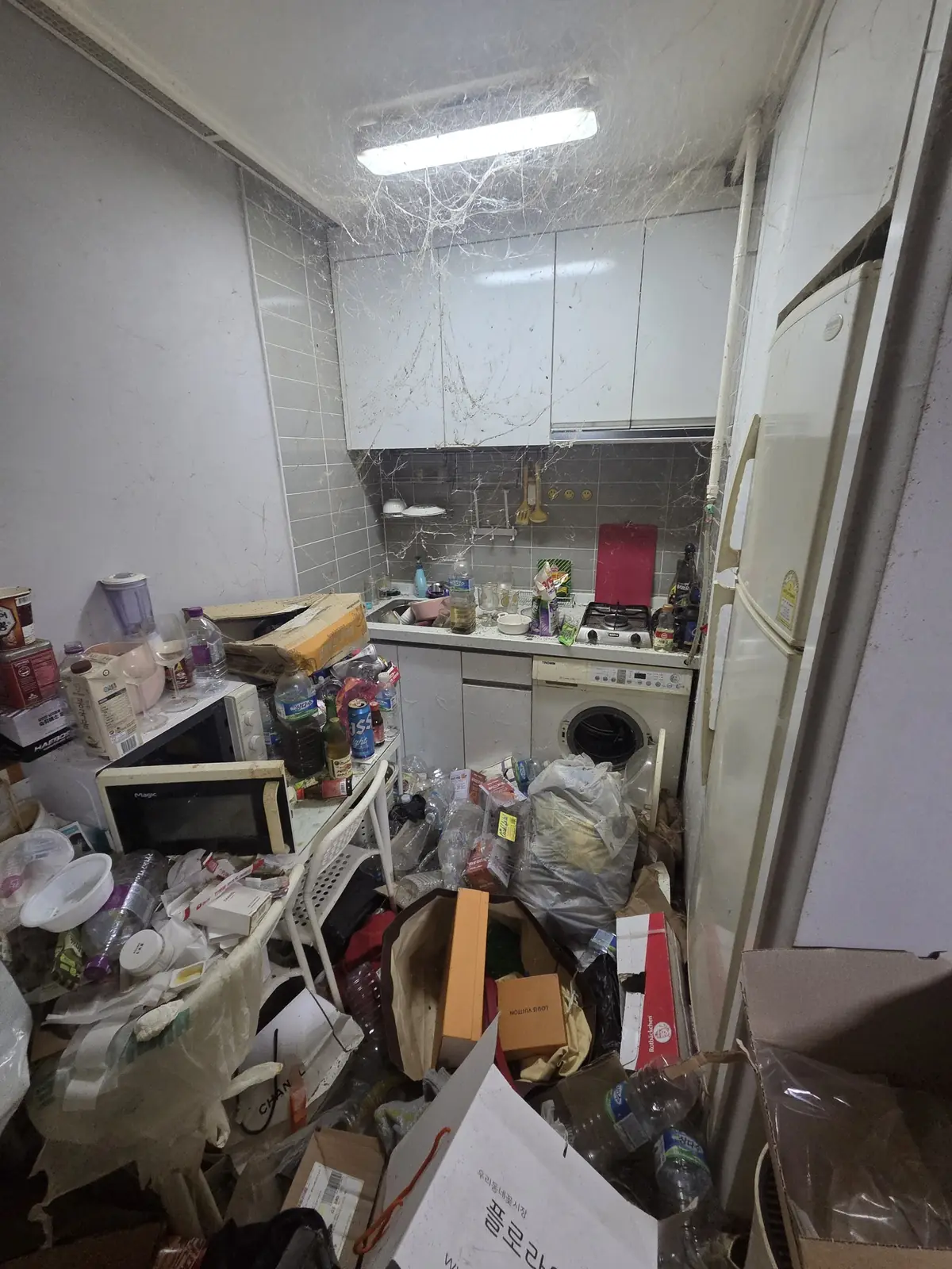 상부장과 천장까지 거미줄이 늘어지고 조리대와 바닥이 음식물 포장재로 뒤덮인 주방 작업 전 상태