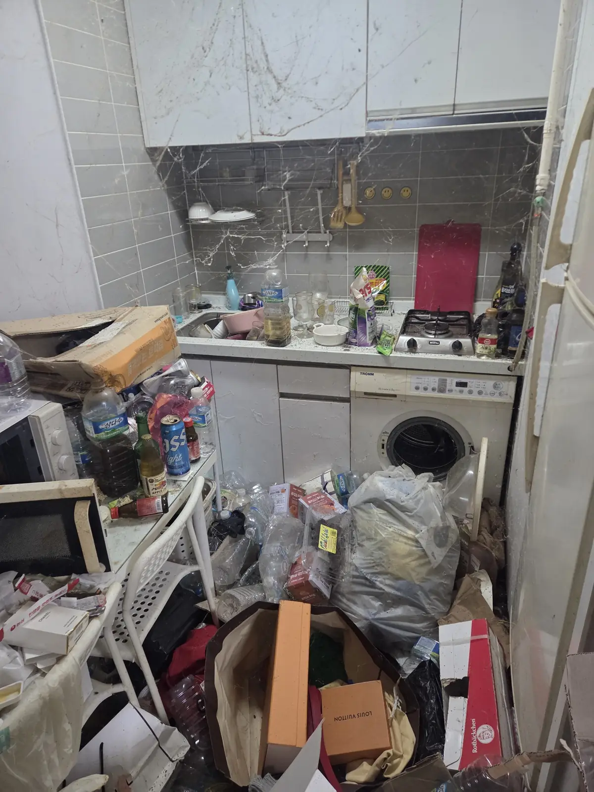 싱크대와 가스레인지 주변에 음식물 잔여물과 병·용기가 쌓이고 벌레 흔적이 남은 주방 근접 상태