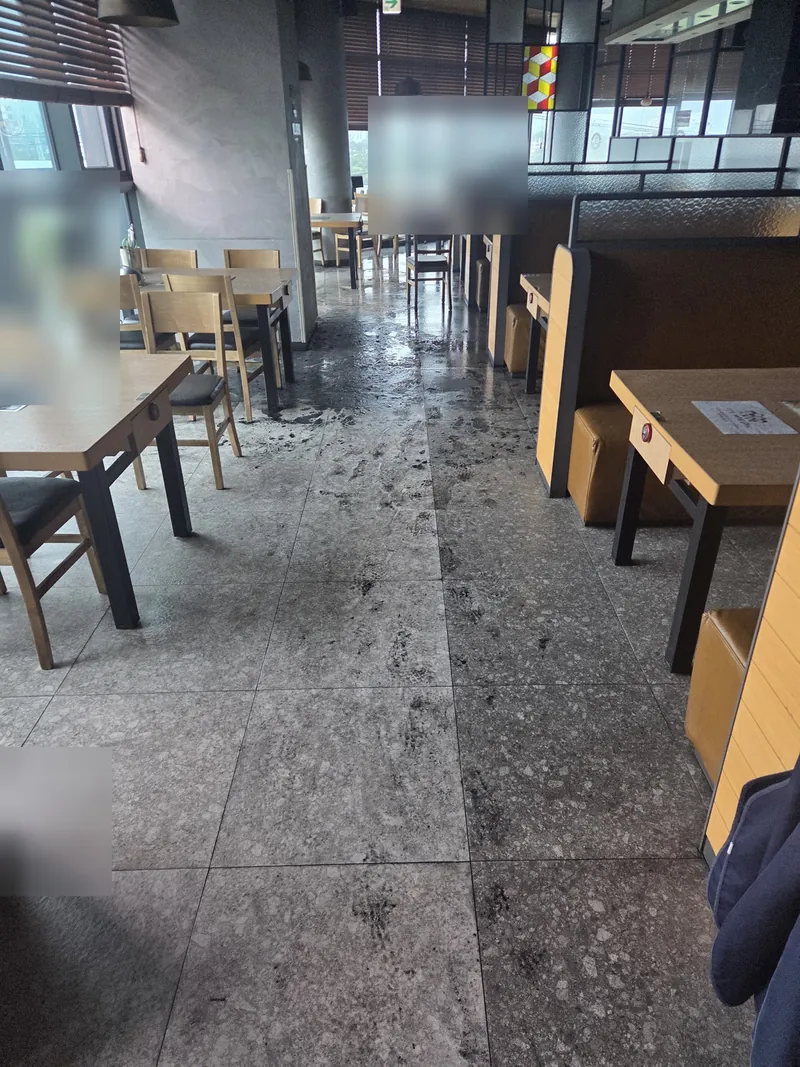 식당 화재 진화 후 소방수와 그을음이 섞인 검은 오염수가 홀 바닥에 퍼지고 통로를 따라 발자국 궤적이 남은 작업 전 상태
