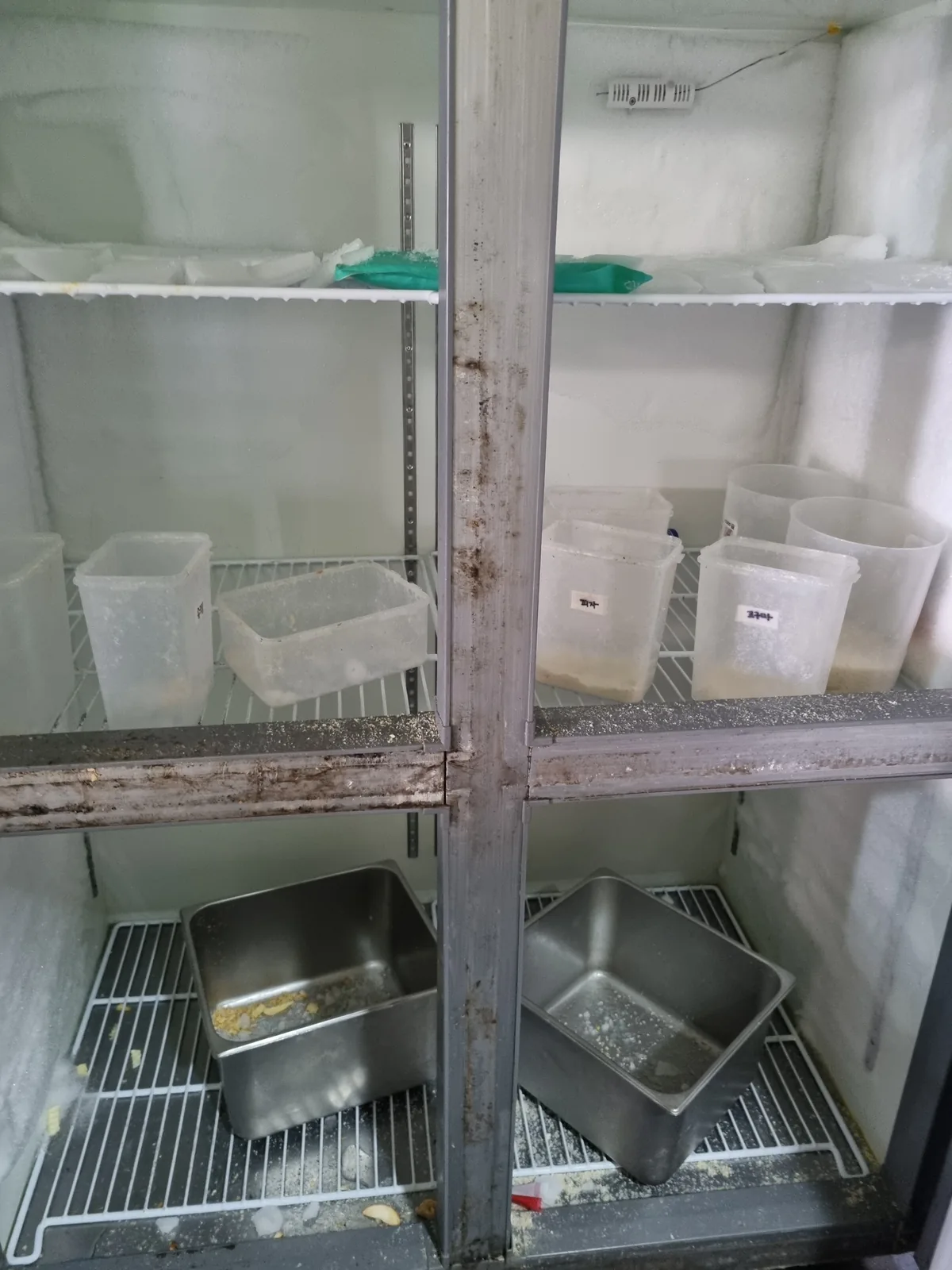 식당 업소용 냉동고 내부 성에와 바닥에 떨어진 식자재 잔여물 — 정리 전 상태