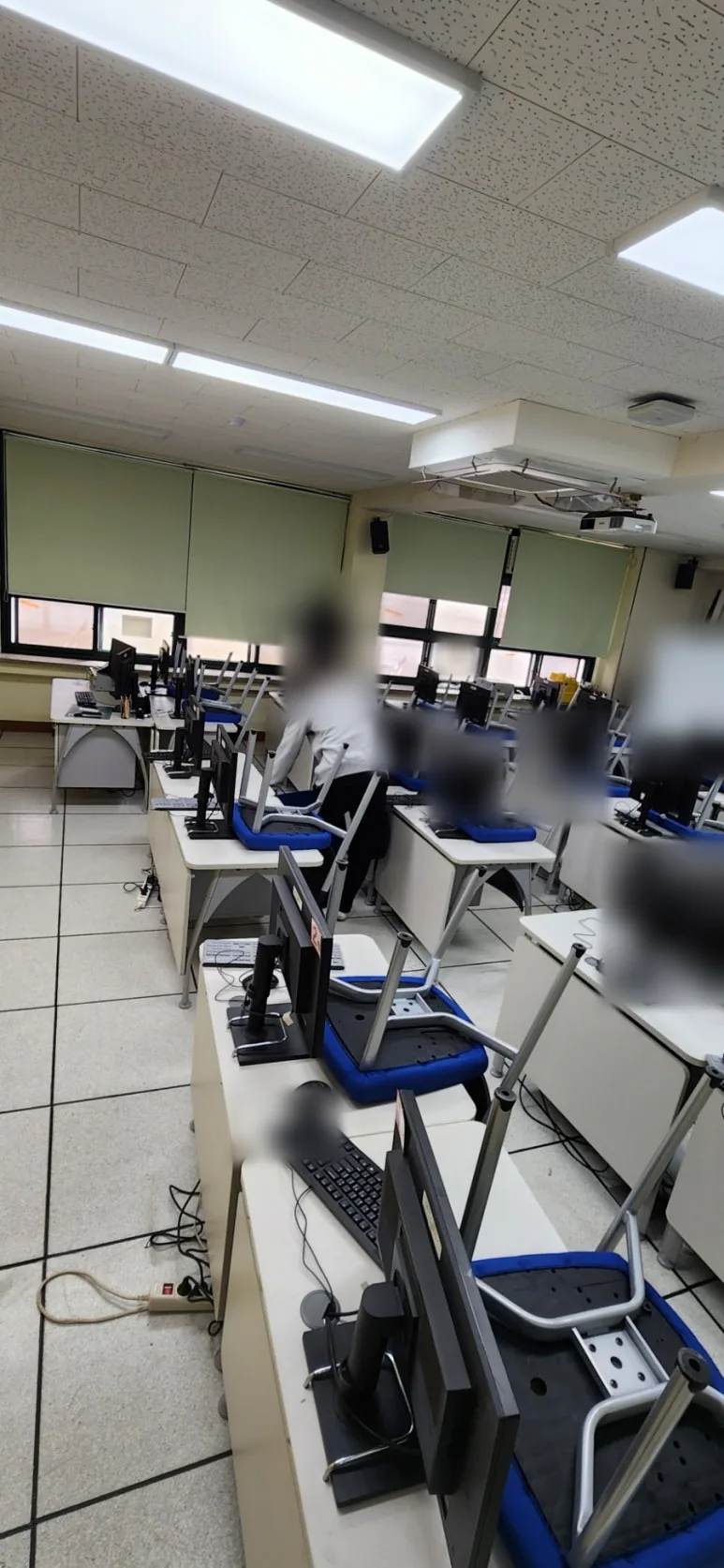컴퓨터실 책상마다 파란 의자를 뒤집어 올려 바닥을 비우고 작업자들이 안쪽 창가와 책상 줄을 정리하는 모습