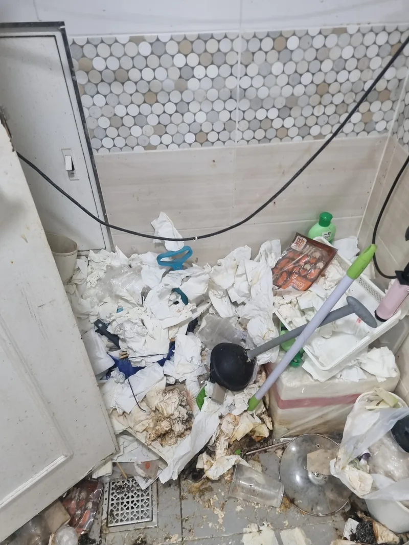 화장실 바닥에 휴지와 생활 쓰레기가 쌓여 배수구까지 막힌 상태 — 물이 빠지지 않아 오염이 고인 현장