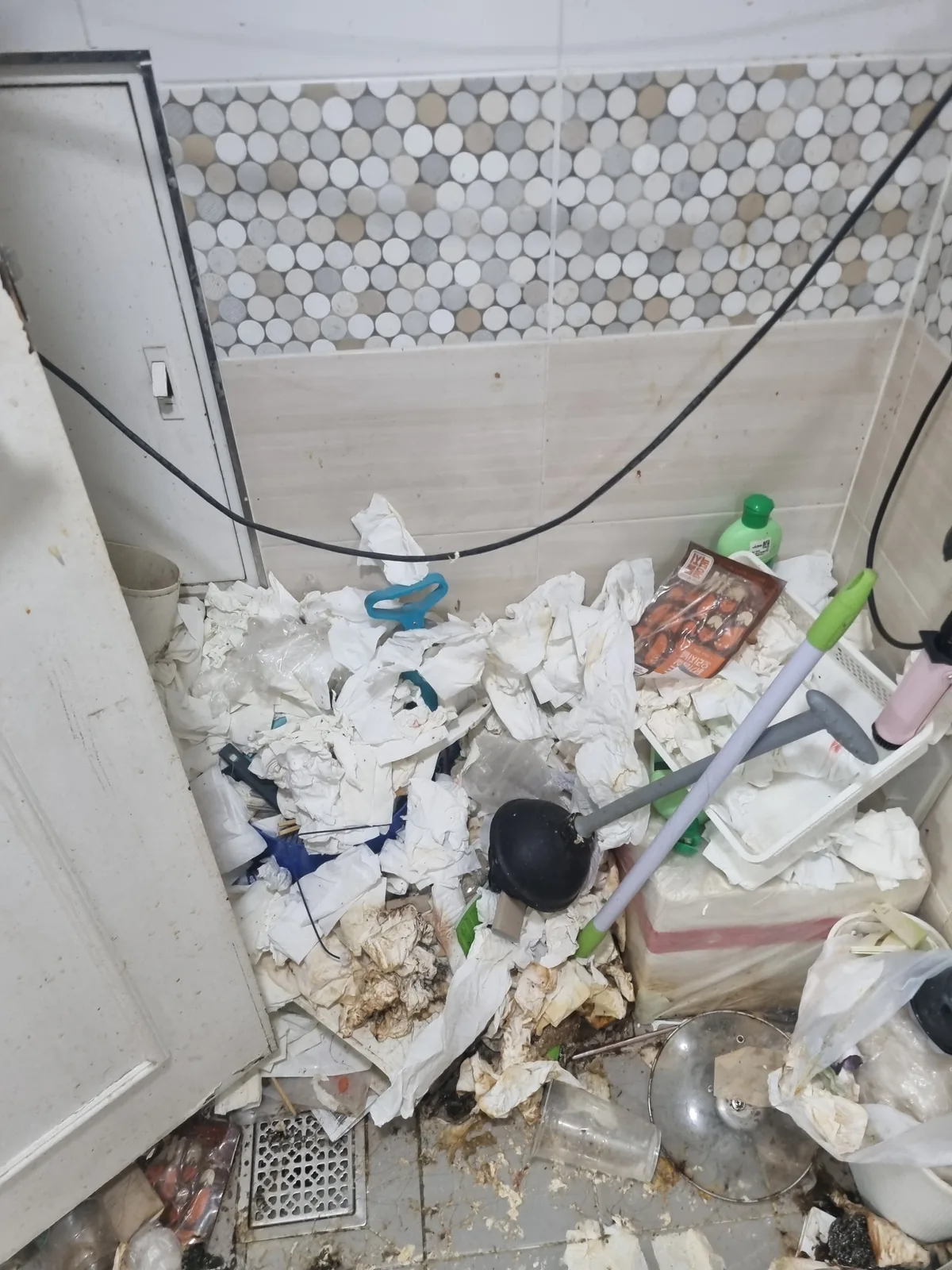 화장실 바닥에 휴지와 생활 쓰레기가 쌓여 배수구까지 막힌 상태 — 물이 빠지지 않아 오염이 고인 현장