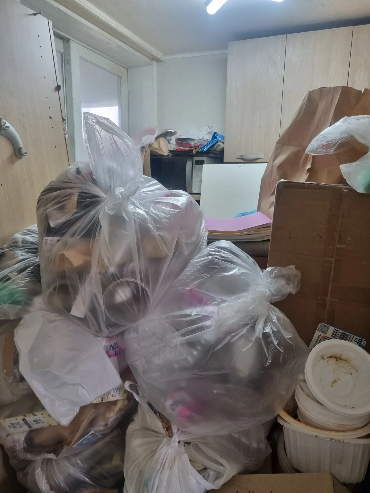주방 앞 통로에 담아둔 봉투가 쌓여 이동이 막힌 상태 — 반출 전 정리 단계