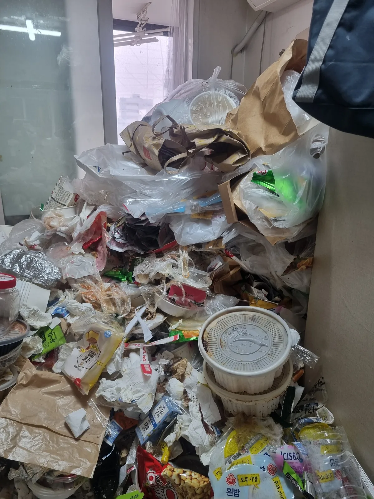 방 전체가 배달 용기와 포장재로 덮여 바닥이 보이지 않는 상태 — 창가까지 쌓인 쓰레기 산